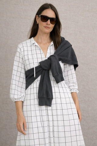 Model trägt das weisse Jeanne Kleid mit dem feinen gewobenen schwarzen Raster im Muster. Zusammen mit einem Sweater von American Vintage