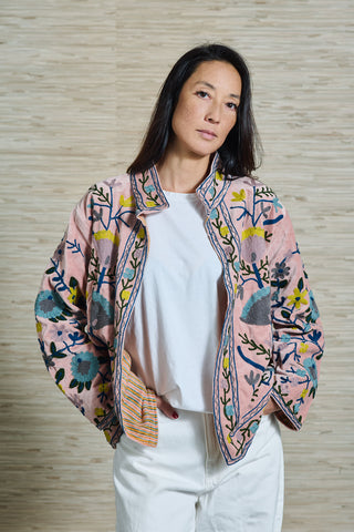 Model Vivienne trägt eine wunderschön bestickete rosafarbene Samtjacke. Die floralen Stickereien sind in türkis, gelb und hellblau.