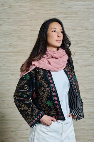 Ein Model trägt eine schwarze bestickte Samtjacke, einen rosa Cashmere Schal  der Schweizer Marke AYRE, und darunter ein weisses Shirt und eine weisse Hose. Die Jacke ist aus Baumwoll Samt und ist wunderschön bestickt. Tragbar im Winter und Sommer.