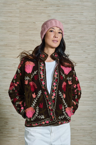 Das Model Vivienne trägt ein Samtjacke mit Stickereien. Die Jacke ist braun und hat pinke und orangene Blumen gestickt, vorne ist sie offen und hat keinen Verschluss. Wie ein Cardigan aber als Jacke. 