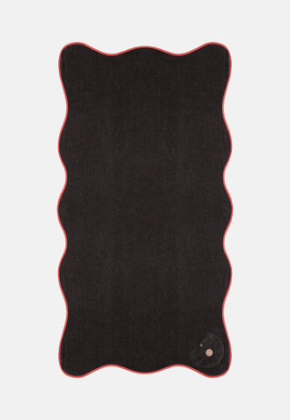 man sieht ain dunkelbraunes fast schwarzes Badetuch mit einem gewellten Rand. Es sieht bequem und verspielt aus, macht gute Laune zum Baden.