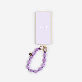 ein violetter bonbon keychain der marke ayre welcher wie hier auch als handykette genutzt werden kann an einer lila handy hülle 