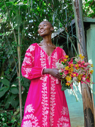 model is wearing the caraine dress from ayre in a pinkberry color with silk stitches and smileys with a bunch of flowers in her hand