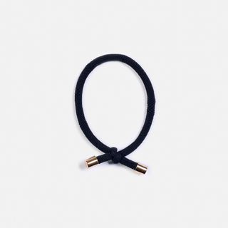 man sieht ein Haargummi in Schwarz mit goldenen Enden. Es hat einen Knoten und ist von der Schweizer Marke AYRE.