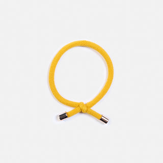 Man sieht das gelbe Haargummi FLIP der Schweizer Marke AYRE. Ein elastisches Gummi mit einem Knopf und goldenen Enden.