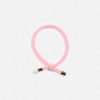 Ma sieht eine Nahaufnahme des Haargummi FLIP der Schweizer Marke AYRE.  Ein geknotetes Haargummi mit goldenen Details am Ende.