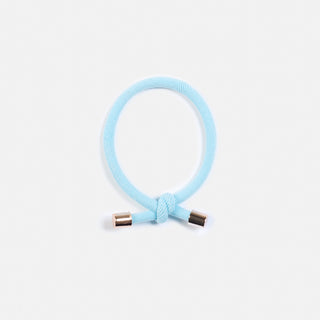 man sieht ein leuchtend hellblaues Haargummi mit einem Knopf und goldenen Enden. Es heisst Flip und ist von der Schweizer Marke AYRE.