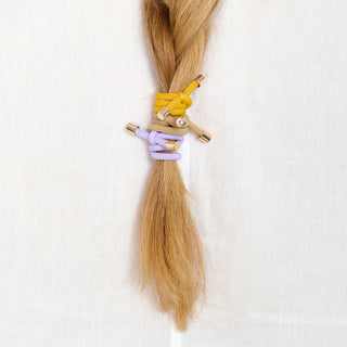 Man sieht einen Haarzopf mit drei Haargummis der Schweizer Marke AYRE. Die Haargummmis heissen Flip und sind hier in den Farben ilac, beige und mustard zu sehen.