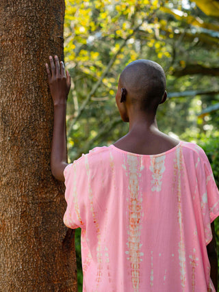 frau von hinten die an einen baum lehnt in einem schoenen pinken tie dye kleid von ayre