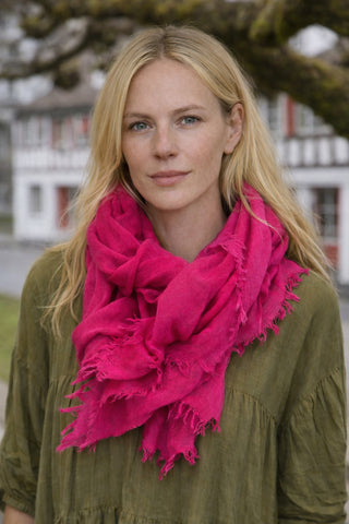 Das Model steht draussen mit dm MAUDE Kleid in der Farbe olive und dem MALIN Schal in der starken Farbe pink.