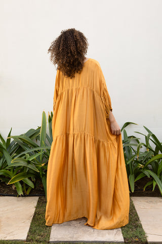 man sieht das maude kleid von hinten. ein weites langes luftiges kleid in der farbe terre, ein gelbliche farbe. das kleid ist von der schweizer marke ayre. 