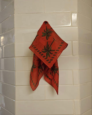 Man sieht das Foulard an einem Haken im Bad aufgehängt. In der Farbe rot, mit grünen Palmen drauf.