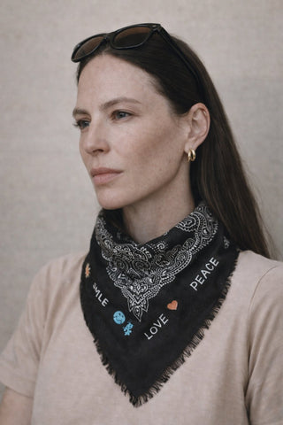 Model trägt einen schwarzen Wolle Schal mit Paisley Muster und lustigen Smiley, Love und Peace Stickereien am Rand herum. Ein Schal der gute Laune macht.