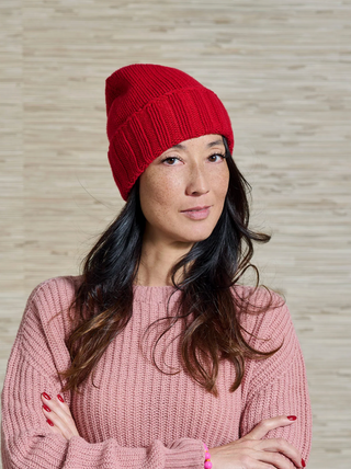 Model trägt eine knallrote Kaschmir Mütze der Schweizer Marke AYRE. Und einen rosa farbenen Kaschmir Pulli mit Rip Optik. Ebenso von der Marke AYRE.