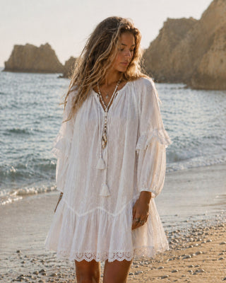 Model trägt am Strand das OPHELIE Kleid der Schweizer Marke AYRE. Ein kurzes romantisches weisses Kleid. 