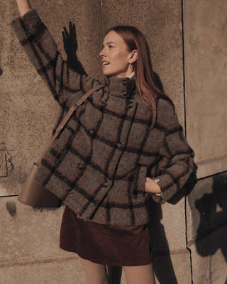 Model trägt die karierte Jacke Plumeria in den Farben grau rot und dunkelgrau. Eine doppelreiher Jacke aus Wolle mit einem schönen klassischen Karomuster. 