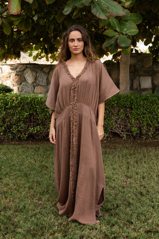Fliessendes Maxikleid aus 100 % Baumwoll-Musselin im warmen Mocca-Ton. Weite Silhouette mit V-Ausschnitt, strukturierter Zierkante und vertikaler Textur. Leicht, atmungsaktiv und vielseitig – ideal für Sommer, Reisen und moderne Resortlooks. One Size.