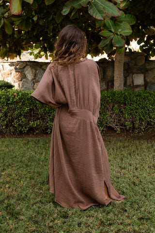 Fliessendes Maxikleid aus 100 % Baumwoll-Musselin im warmen Mocca-Ton. Weite Silhouette mit V-Ausschnitt, strukturierter Zierkante und vertikaler Textur. Leicht, atmungsaktiv und vielseitig – ideal für Sommer, Reisen und moderne Resortlooks. One Size. (backside)