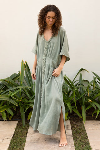 Fliessendes Maxikleid aus 100 % Baumwoll-Musselin in einem ruhigen Seagrass Ton. Weite Silhouette mit V-Ausschnitt, strukturierter Zierkante und vertikaler Textur. Leicht, atmungsaktiv und vielseitig – ideal für Sommer, Reisen und moderne Resortlooks. One Size.