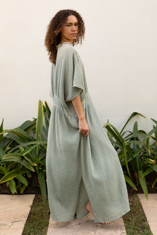 Fliessendes Maxikleid aus 100 % Baumwoll-Musselin in einem ruhigen Seagrass-Petrolton. Weite Silhouette mit V-Ausschnitt, strukturierter Zierkante und vertikaler Textur. Leicht, atmungsaktiv und vielseitig – ideal für Sommer, Reisen und moderne Resortlooks. One Size. (backside)