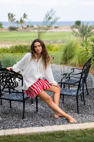 Leichte Baumwollbluse in klarem Weiss mit tonaler Strukturstickerei. Weite, fliessende Silhouette, puristischer Stehkragen und dezente Punkttextur. Atmungsaktiv, weich und vielseitig kombinierbar – ideal für Sommer, Reisen und moderne Alltagslooks. One Size. Moodbild Model trägt Vick-Rock sitzt auf Stuhl.