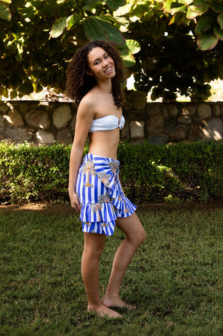Model steht seitlich im Wickelrock aus Baumwolle, gestreift blau weiss mit einem Palmenprint drauf. 